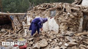 Woman in purple sifts through rubble - BBC News